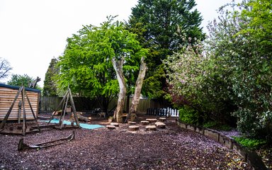 A children's play area with natural stepping stones, wooden structures and trees around the outside