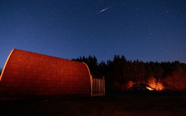A camping pod in the dark with a shooting star in the sky