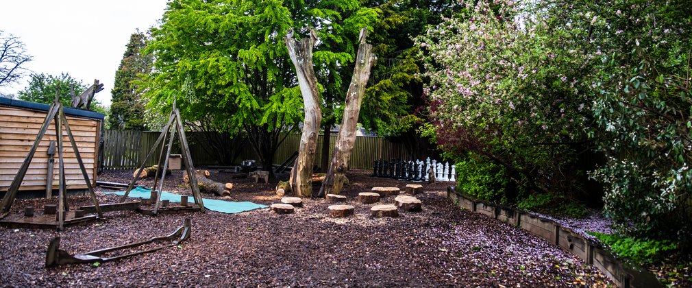 A children's play area with natural stepping stones, wooden structures and trees around the outside