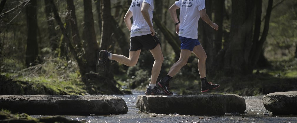 two runners crossing a stream on a running trail in the forest