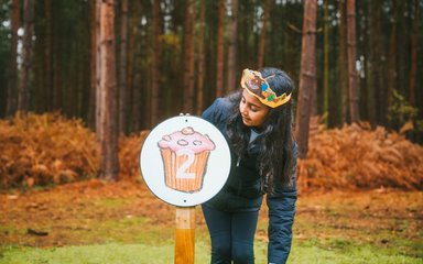 Girl in forest pointing at cupcake panel
