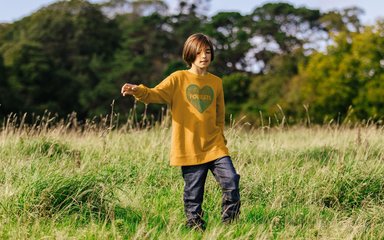 Boy in a mustard sweatshirt waling in a field