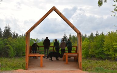 A group of people stand in a timber structure looking across the countryside