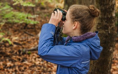 close-up of a girl looking through binoculars in the forest