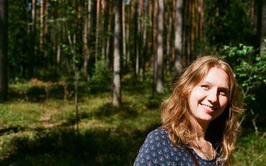 Fair haired woman smiles in the sunlight, with a forest backdrop
