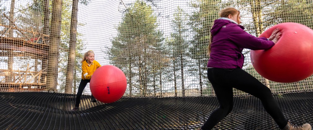 A child and an adult playing with exercise balls in the Go Ape Nets Adventure enclosure above the ground.