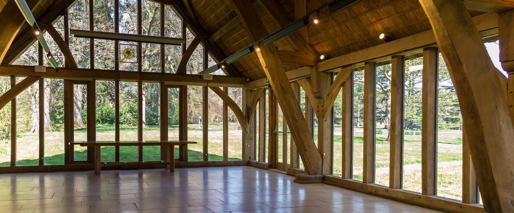 The inside of a wooden building called the Great Oak Hall. Glass sits between beams of light brown wood to look out on to a landscape of trees.