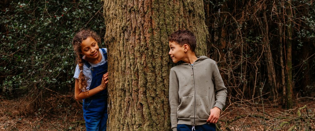 Two children looking at each other round a tree