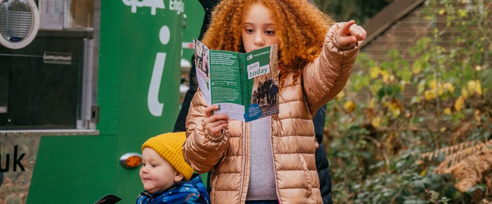 A girl is holding a Forestry England leaflet and pointing to something. A woman and young boy are with her.