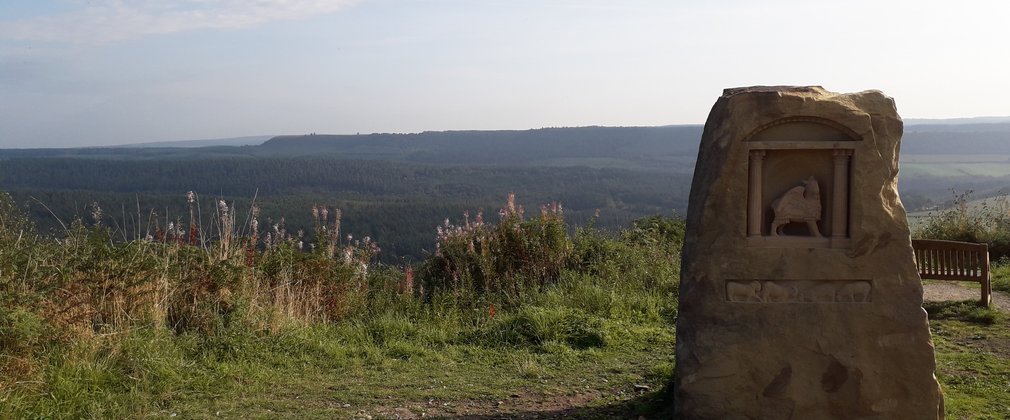 Photograph of winged sheep sculpture with view across forest land 