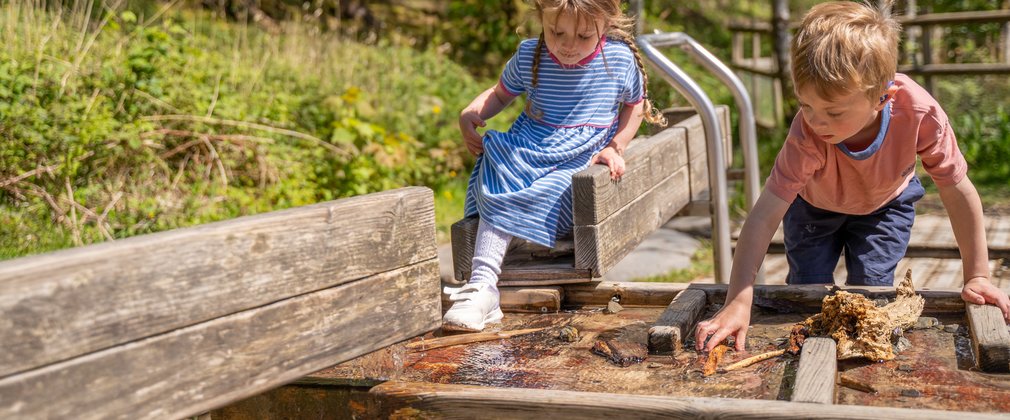 A girl and a boy playing with a piece of outdoor play equipment