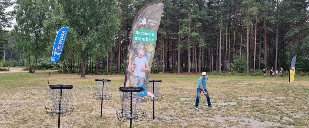 Man throwing at disc at a disc golf basket in a forest