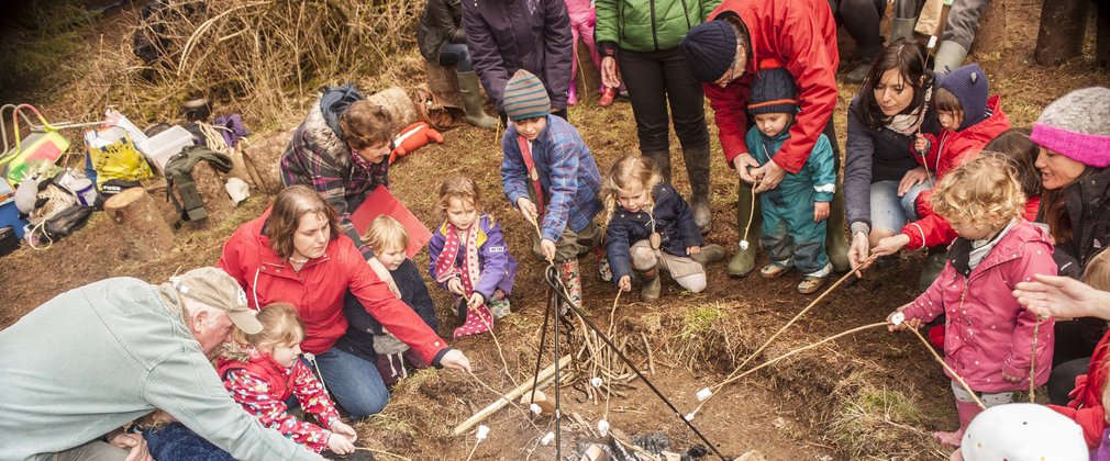 Children and parents are gathered round a campfire toasting marshmallows