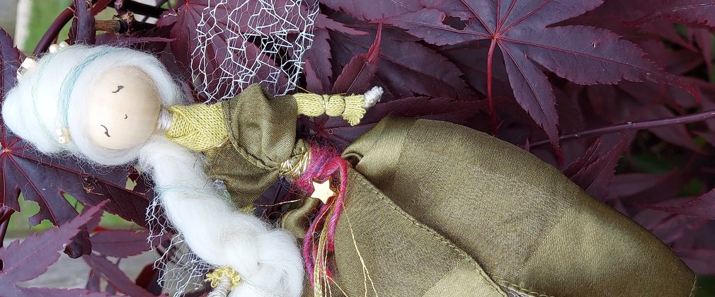 A scrap crafted fairy sits on a bed of purple leaves
