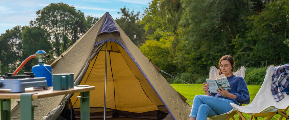 A woman reading sat next to a tent