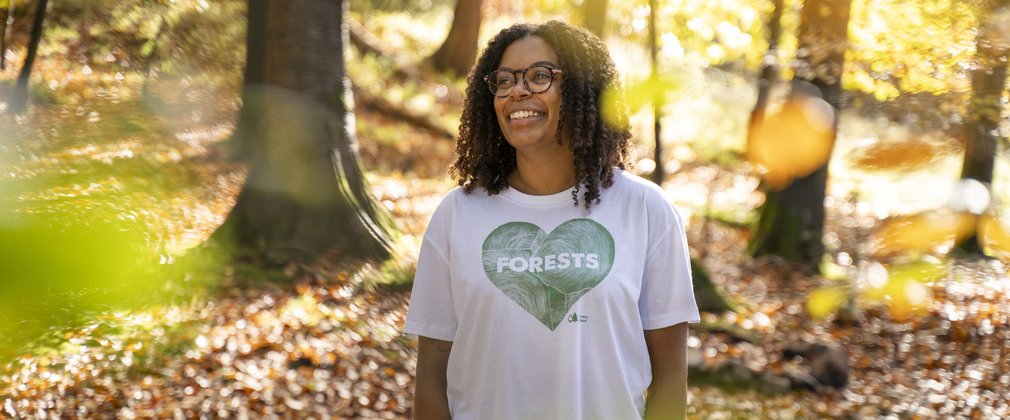 Woman wearing a white t-shirt with a green heart on it in a forest