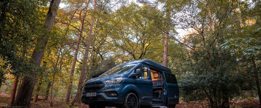 A campervan surround by autumnal trees at a campsite