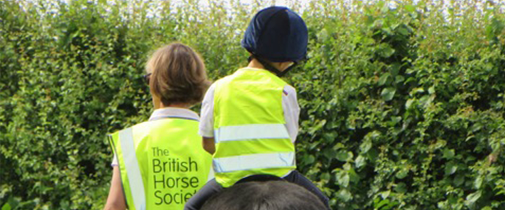 Adult in The British Horse Society high vis walking a child on a horse