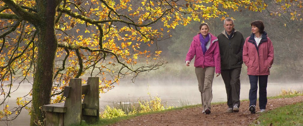 walkers enjoying a walk around a woodland lake in autumn 