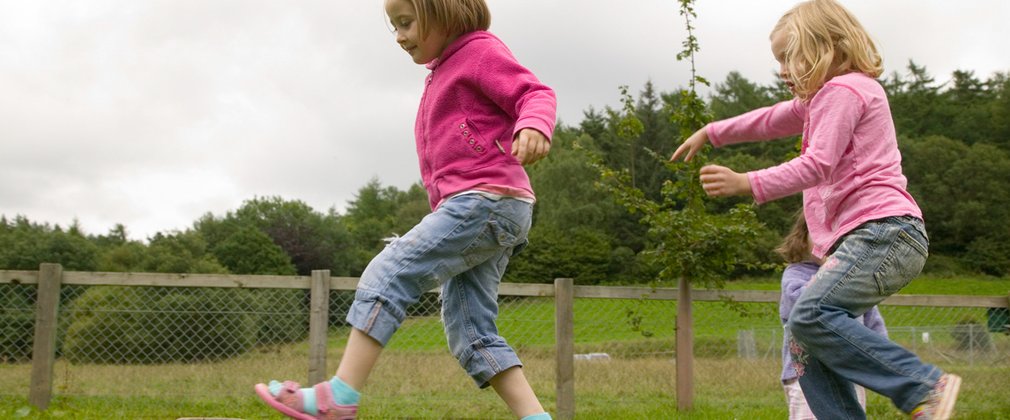 children balancing on wooden beam in play area in the woods