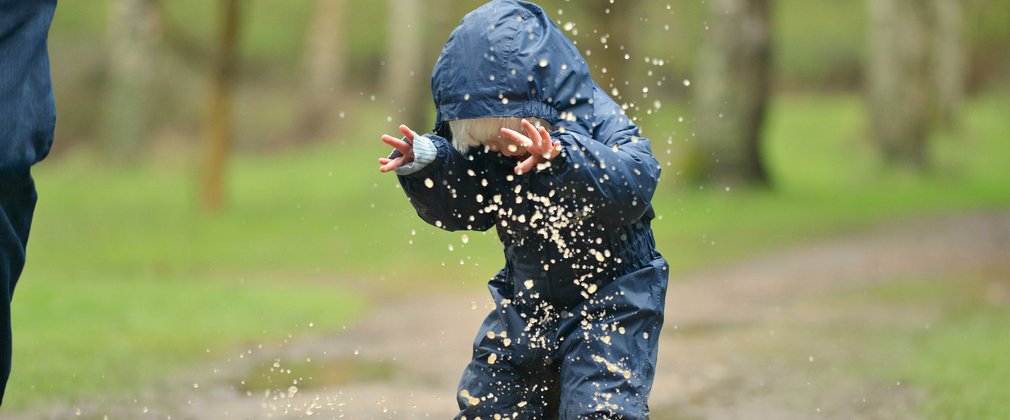 Child jumping in puddle and being splashed in the face 