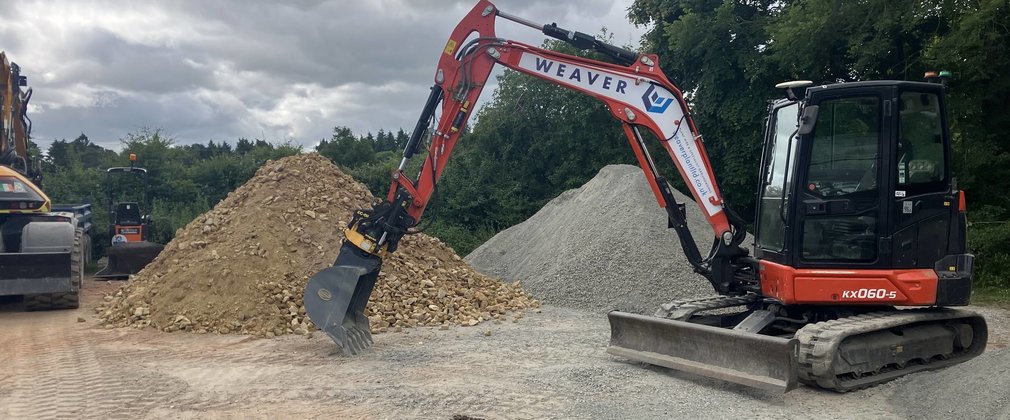 A digger on a forest trail in front of a pile of surfacing material