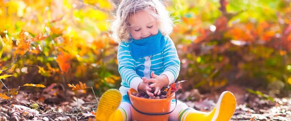 Young girl playing with a bucket of autumn leaves