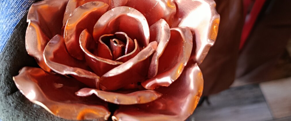 A metal rose in a workshop being bent into shape with a pair of pliers