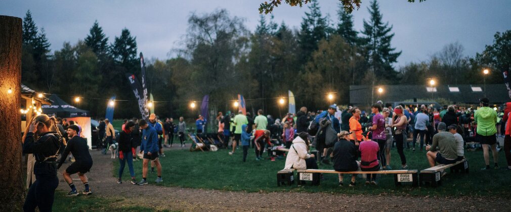 Large group of people gathering in a forest setting for a running event at twilight