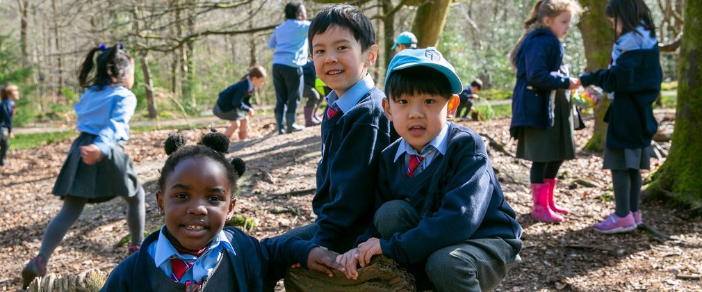 Children in the foreground sat on a log while children in the background explore the forest