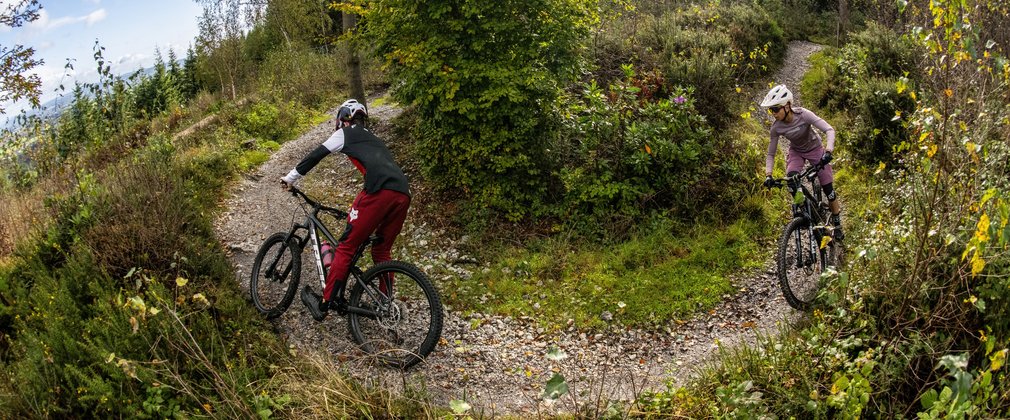 Two mountain bike riders through a turn on a singletrack forest trail