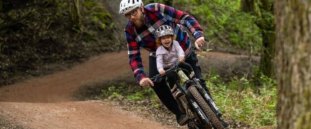 Man and child sharing a bike on a mountain bike trail