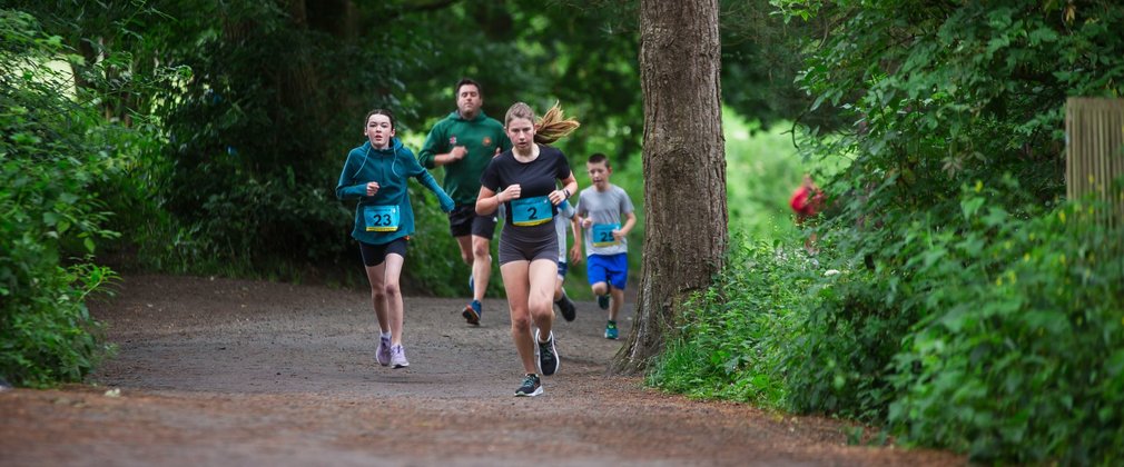 Three young people wearing race bibs running on a forest path