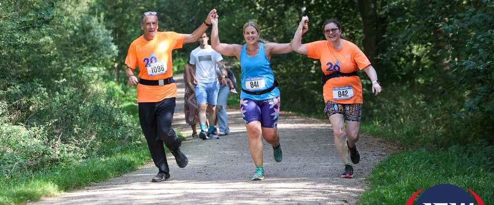 3 people holding hands in the air as they run through a forest