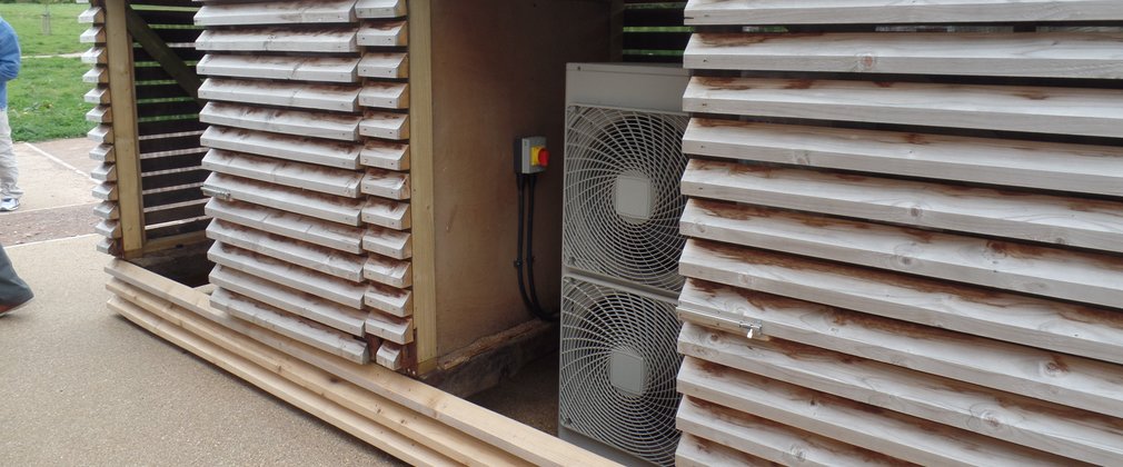 A wooden shed with two fans inside and trees behind