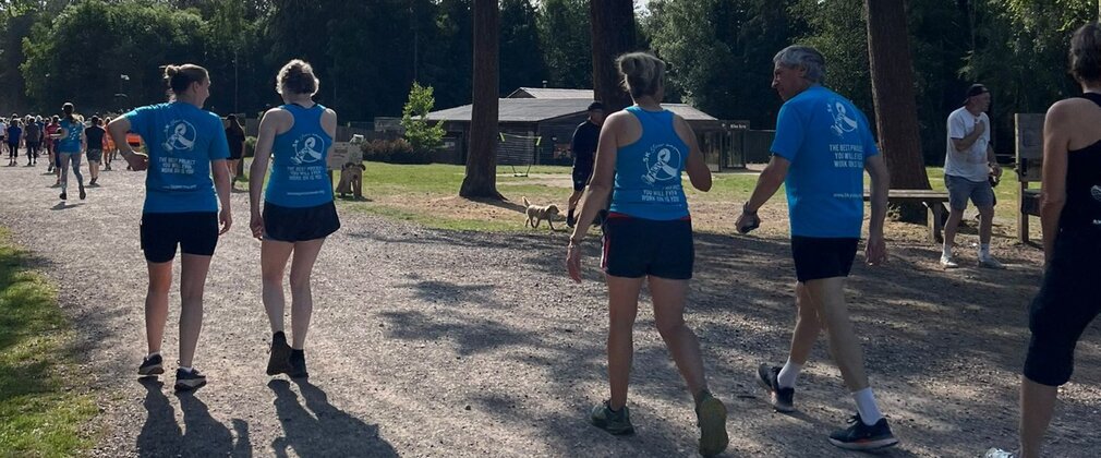 Four people wearing matching sports tops walking on a forest path with their backs to the camera.