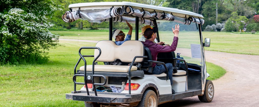 A small shuttle bus drives away from the camera with two visitors waving in the back.