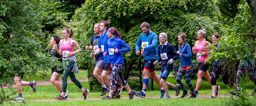 A group of runners are taking part in the Westonbirt 10K surrounded by trees.