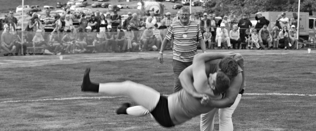 A black and white photo of two people wrestling in a ring with judge and spectators in the background
