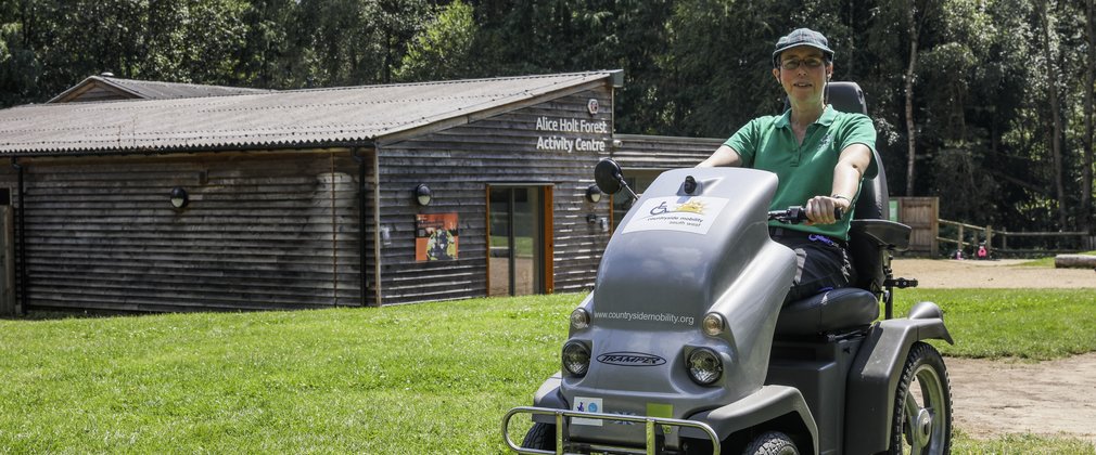A person sitting on an all-terrain mobility scooter in front of the Activity Centre at Alice Holt Forest