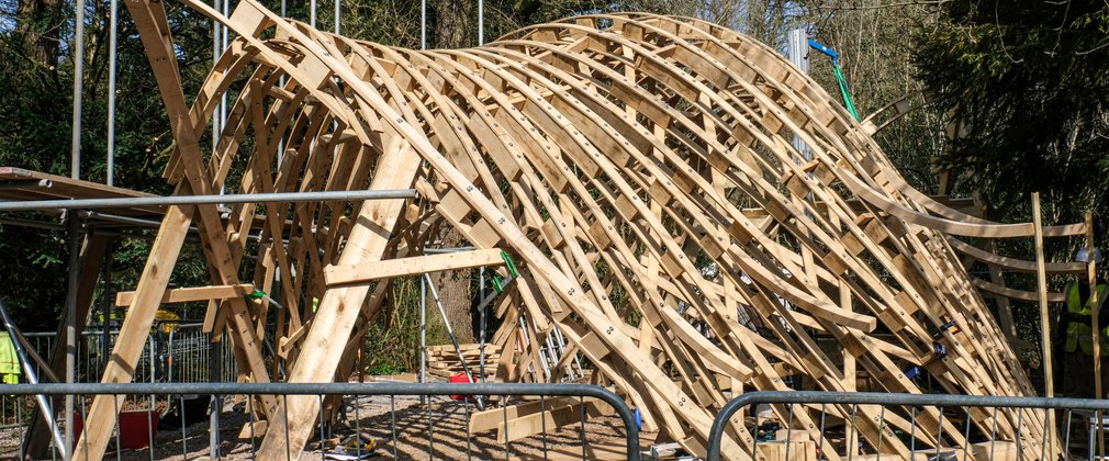 A unique shaped wooden structure made up of lots of wooden arches to create a shelter that people can stand under