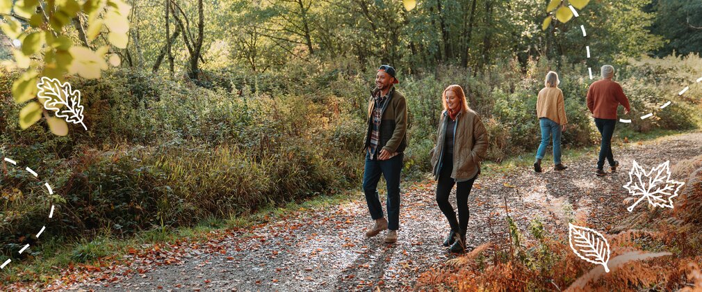Four people walking along a woodland path surrounded by autumn foliage and trees.