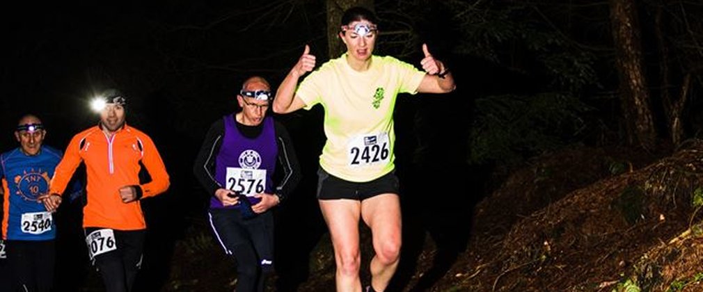 Runners with head torches racing through forest at night