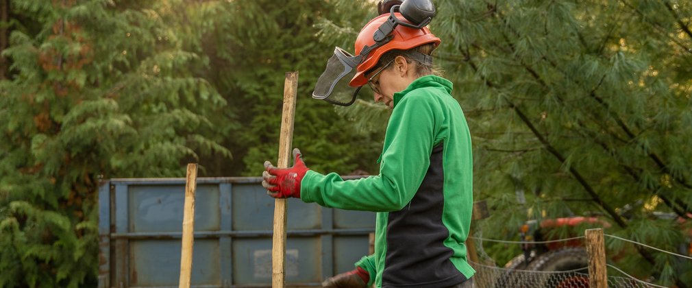 Woman holding wooden stake wearing forestry gear