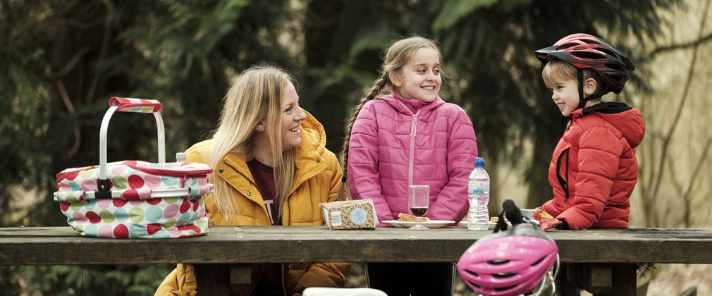 Woman and two children having a picnic on a picnic table in the forest