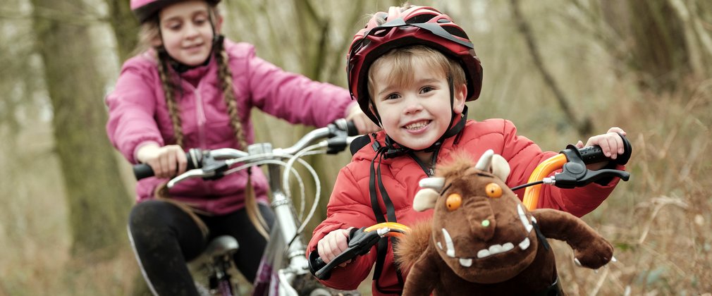 Two children on bikes, one with a Gruffalo toy in the front basket