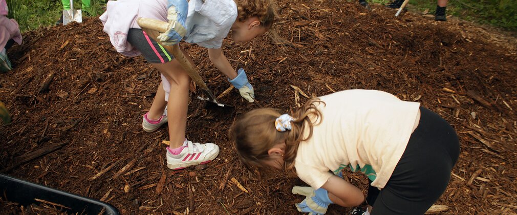 2 young girls crouch down to dig into the soil ready to plant a tree