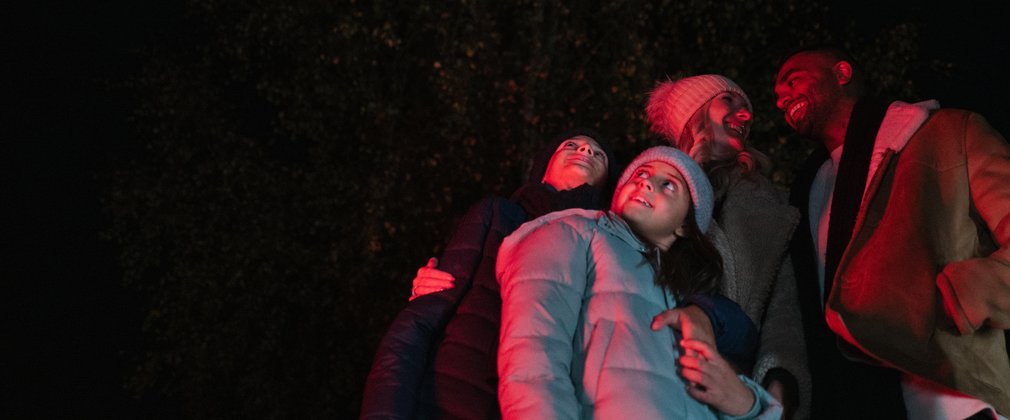 A family huddled together under red lighting looking up at the night sky