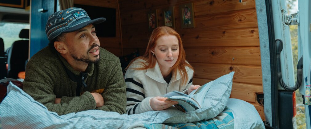 Couple reading a book in a campervan with the back door open