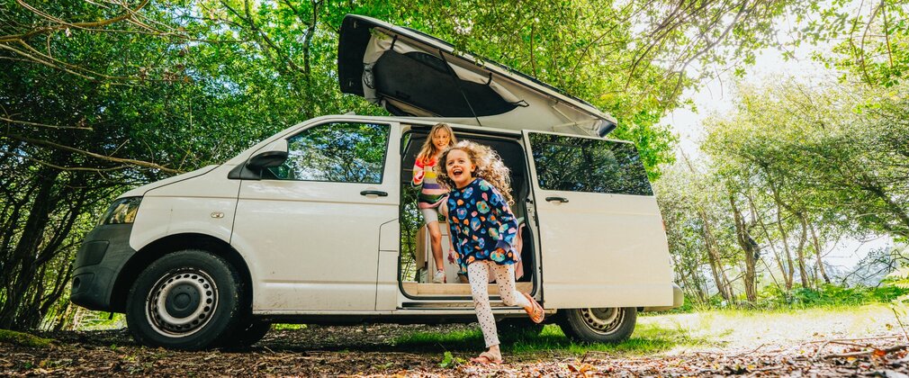 Campervan in the forest with two children running out from an open door